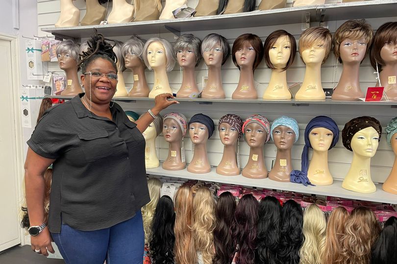 Black lady wearing glasses points at wigs in a hair shop
