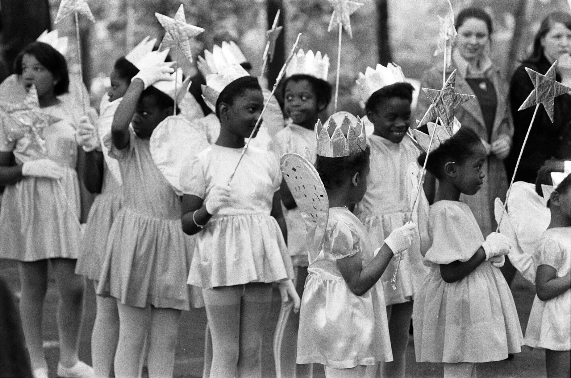 Nine little girls with angel costumes, wands and afro hair styles smile as they take part in the carnival procession